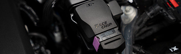 Primer plano de la unidad de control RaceChip S en el compartimento del motor, carcasa negra con logotipo de RaceChip, etiqueta del producto y conector de serie violeta.